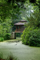 Fototapeta na wymiar a wooden house in a park on a bridge above the water in a green landscape