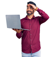 Young hispanic man holding laptop stressed and frustrated with hand on head, surprised and angry...