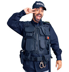 Young hispanic man wearing police uniform doing peace symbol with fingers over face, smiling cheerful showing victory