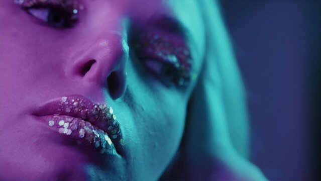 Extreme close up a beautiful blonde girl in a neon studio, sexually opens eyes and mouth. Beauty portrait of a woman face. Female with beautiful make up, glitter shadows and false lashes. Neon light