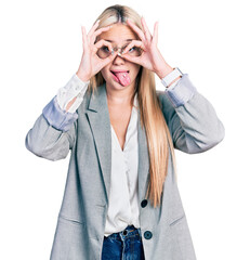 Beautiful blonde woman wearing business jacket and glasses doing ok gesture like binoculars sticking tongue out, eyes looking through fingers. crazy expression.