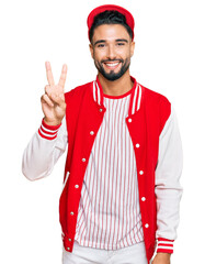 Young man with beard wearing baseball uniform showing and pointing up with fingers number two while smiling confident and happy.