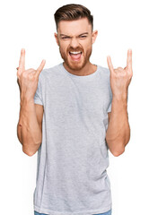 Young redhead man wearing casual grey t shirt shouting with crazy expression doing rock symbol with hands up. music star. heavy concept.