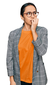 Young hispanic girl wearing business jacket and glasses looking stressed and nervous with hands on mouth biting nails. anxiety problem.