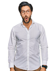 Young hispanic man wearing business shirt and glasses afraid and shocked with surprise expression, fear and excited face.