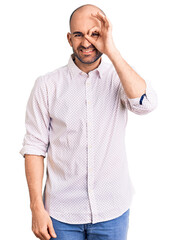 Young handsome man wearing elegant shirt doing ok gesture with hand smiling, eye looking through fingers with happy face.