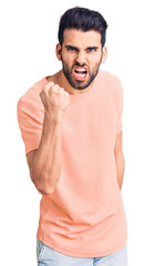 Young handsome man with beard wearing casual t-shirt angry and mad raising fist frustrated and furious while shouting with anger. rage and aggressive concept.