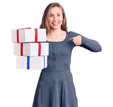 Young beautiful blonde woman holding birthday gift pointing finger to one self smiling happy and proud
