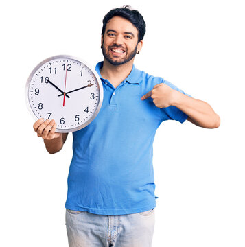 Young hispanic man holding big clock pointing finger to one self smiling happy and proud