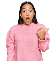 Young asian woman wearing casual winter sweater surprised pointing with hand finger to the side, open mouth amazed expression.