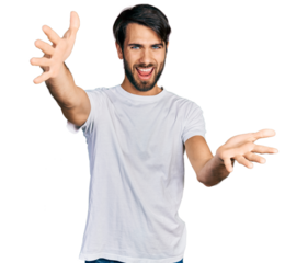 Hispanic man with blue eyes wearing casual white t shirt looking at the camera smiling with open arms for hug. cheerful expression embracing happiness.