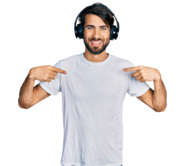 Hispanic man with blue eyes listening to music using headphones looking confident with smile on face, pointing oneself with fingers proud and happy.