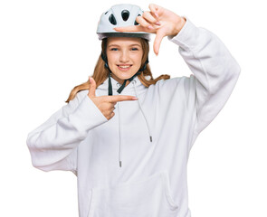 Beautiful young caucasian girl wearing bike helmet smiling making frame with hands and fingers with happy face. creativity and photography concept.
