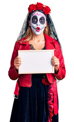 Woman wearing day of the dead costume holding empty white chalkboard scared and amazed with open mouth for surprise, disbelief face