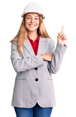 Beautiful young woman wearing architect hardhat with a big smile on face, pointing with hand and finger to the side looking at the camera.