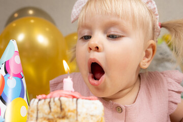 A two-year-old girl blows out a candle on a birthday cake, makes a wish
