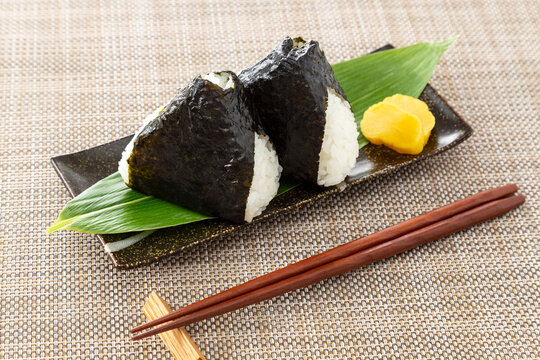 ランチョンに置かれたおにぎり, おむすび, 握り飯, 白米, お米, 和食, 昼食, ランチ, 軽食, ご飯, たくあん, たくわん, 海苔, 米, ごはん, 食べ物, 日本食, 食事, のり, 手作り, ブツ撮り, 物撮り, 人なし, 人無し, ひとなし, 無人, 人物無し, 人物なし, コピースペース, 皿, ランチョンマット, 白, 茶色, 孤立した, おいしい