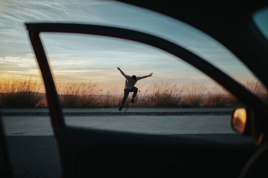 Skater performing trick on skateboard on asphalt road in sunset