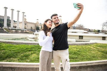 Naklejka premium Happy young couple taking a selfie with phone in park. Cheerful couple smiling and taking a picture outside.