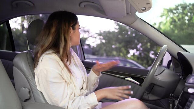 Young beautiful brunette turns on radio in her car, listens to music, dances and enjoys her favorite songs.