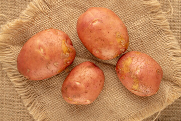 Four raw pink potatoes  on jute cloth, top view.