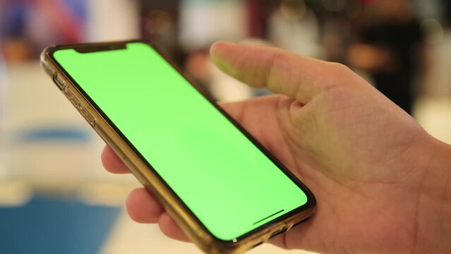Female hand using smartphone green screen outside on blurred background, close up. Online chat, internet purchase, browse web, download new freeware application. 