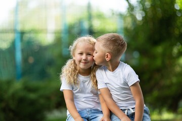 Beautiful little girl kissing his friend on natural park background.