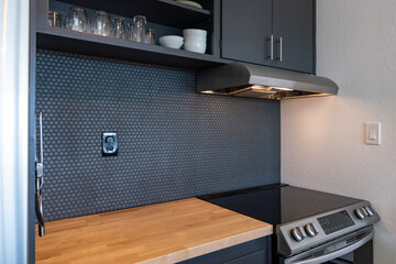 Modern kitchen details of electric stove with tiny blue tile backsplash, dark blue cabinets and...