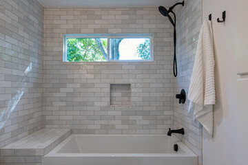 Detail of new tile shower with black faucets, deep tub and picture window. 