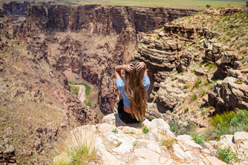Back view of girl on a steep cliff taking in the amazing view over famous Grand Canyon on a beautiful sunny day, Grand Canyon National Park, Arizona, USA