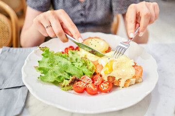 Woman cuts poached egg and yolk flows out. Brioche, avocado cream with salmon and egg . Healthy breakfast, protein. Restaurant dish. 
