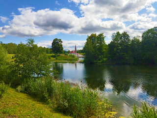 Fototapeta premium Summer landscape with lake and Romantic castle with tower and red roof. Priory Palace in Gatchina in Leningrad region, near St. Petersburg, Russia.