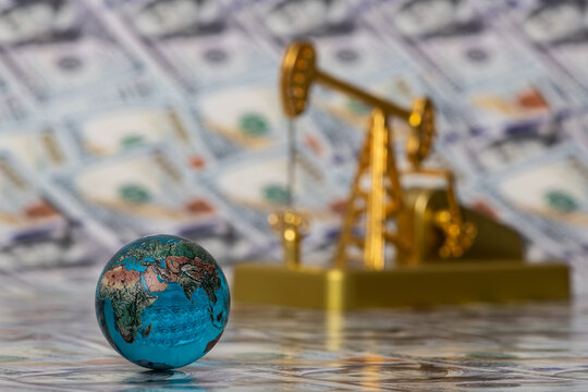 Golden oil pump and glass globe against the background of 100 US dollar bills