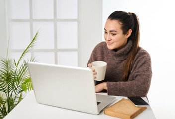 Fototapeta premium young girl with a cup of coffee in her hand performing tasks on the computer