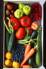 Wooden crate full of healthy seasonal fruit and vegetable. Top view, dark background.