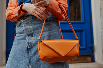 Street fashion details: woman wearing trendy summer outfit, carrying orange color faux patent...