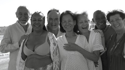 Happy multiracial senior friends smiling on camera during sunset time on the beach - Elderly people having fun together during travel vacation - Black and white editing