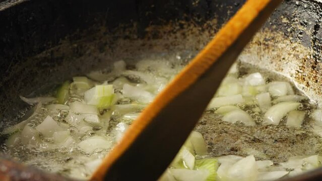 Finely chopped onion fried in a frying pan with asl is mixed with a wooden spatula. Close-up