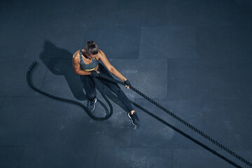 Strong caucasian woman pulling rope top view. Sporty woman in sportswear working out in gym....