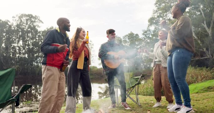 Friends, bonfire and guitar with singing, dancing and happy together in nature, woods or park for holiday. Men, women and excited for freedom, chat and camping by fire for music, forrest and vacation