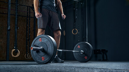 Sportsman performing weight lifting exercise at gym, croped shot, low angle view focus on barbell