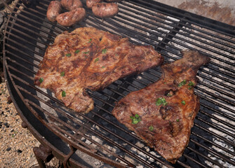Barbecue outdoors. Closeup view of matambre, pork meat and sausages roasting in the grill.	
