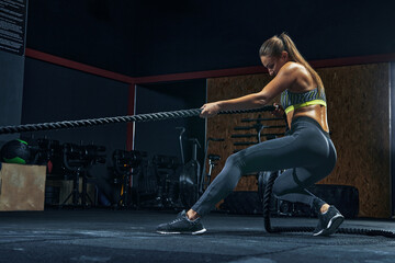 Full-length shot of Power woman functional training with black rope at a gym