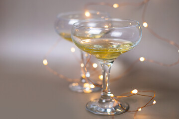 Two glasses of champagne surrounded by a garland on a beige background. Cocktail for the New Year. For the design of cards, invitations, posters, illustrations, presentations, flyers.