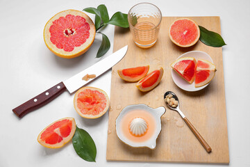 Wooden board with pieces of ripe grapefruit and juicer on white background