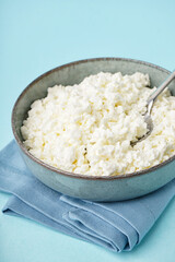 Bowl with tasty cottage cheese on blue background