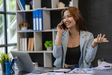 Asian businesswoman holding smartphone in talking with business clients with charts or documents in workplace using calculator, business laptop, financial accountant calculating money, loan bank,