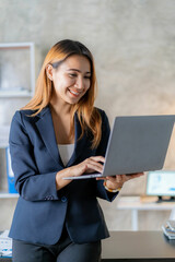 Beautiful Asian businesswoman working with laptop sitting at home. A happy smiling woman is having a meeting with the team online. vertical image