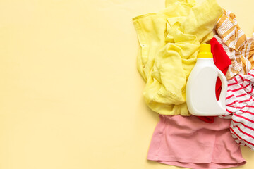 Pile of dirty clothes and bottle of laundry detergent on yellow background