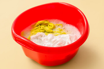 Plastic basin with dirty clothes, water and foam on yellow background, closeup